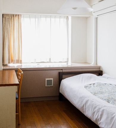 An image of a standard single room equipped with a bed, a desk, and a chair.