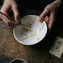 A person holding a paintbrush to mend a broken bowl using gold