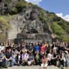 Students taking memorial photos in front of the giant Buddha statue in the mountains with the Deans