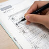 A person writing the kanji character "春" with a pen in a workbook.