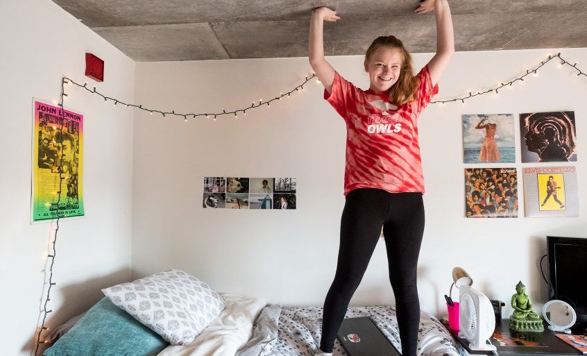 A student standing on her bed in the dorm.