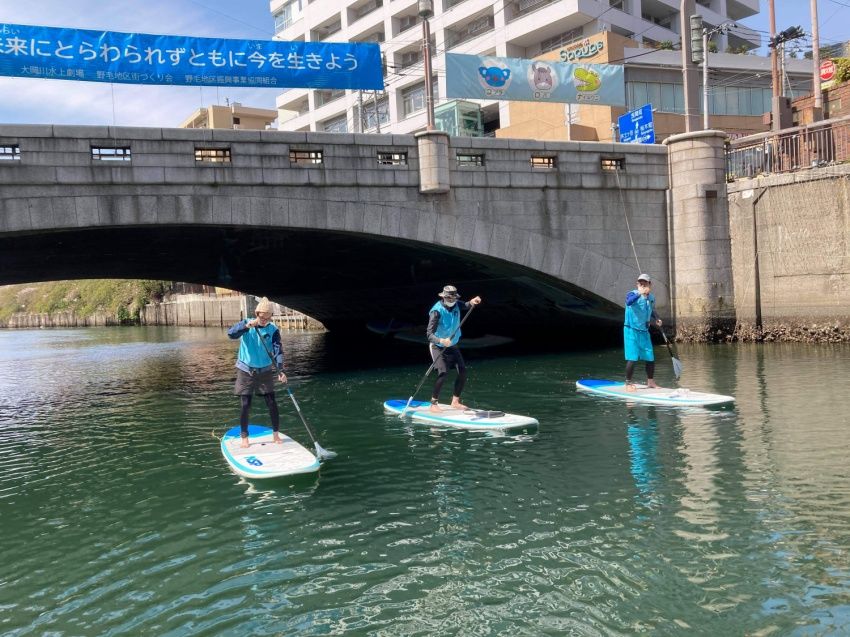 In the picture, three people are on their paddle board while navigating a river